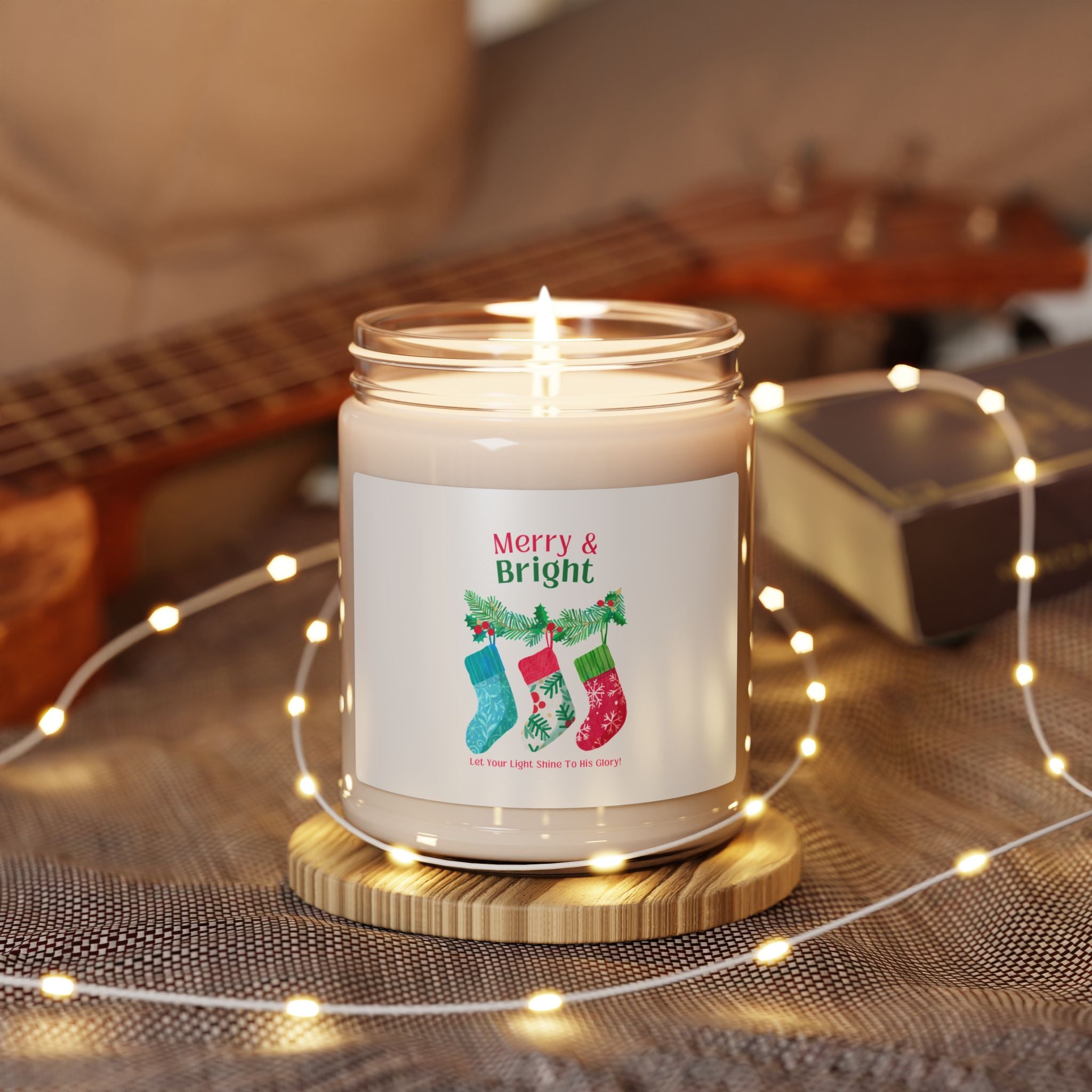 Candle with 'Merry & Bright' label on a wooden coaster surrounded by string lights and a guitar in the background