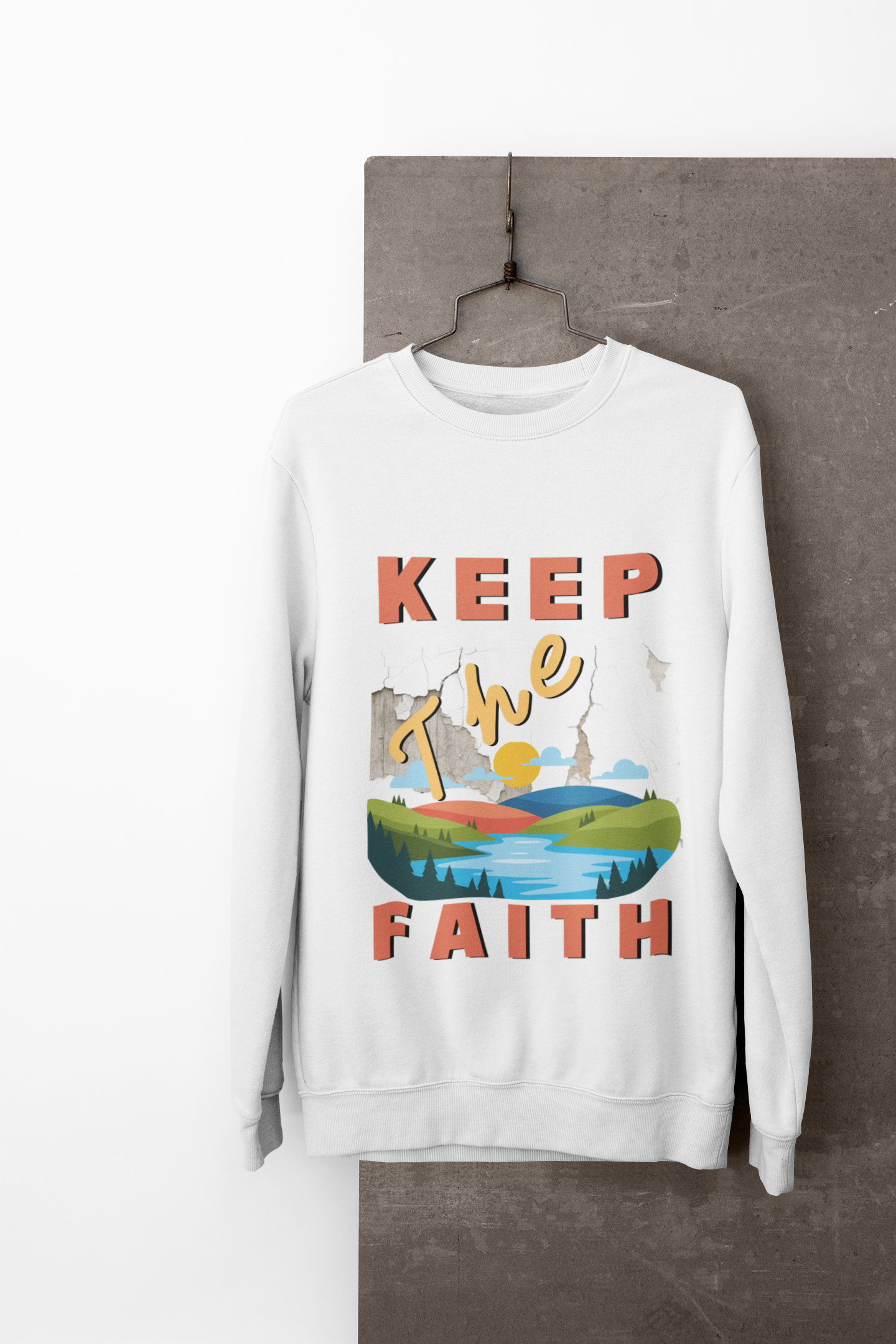 White sweatshirt with 'Keep The Faith' text and landscape design on a hanger against a neutral background