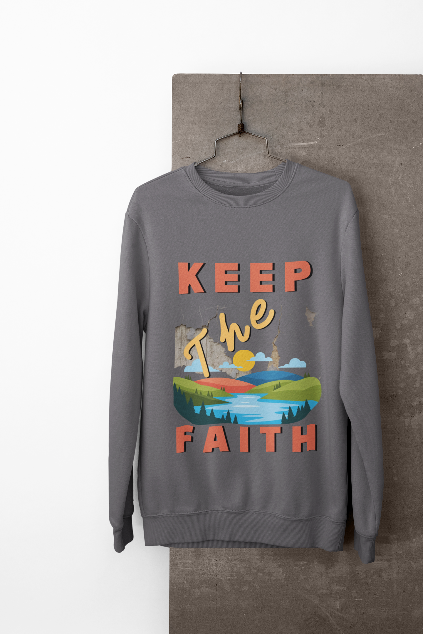 Gray sweatshirt with 'Keep The Faith' text and landscape graphic on a hanger against a neutral background