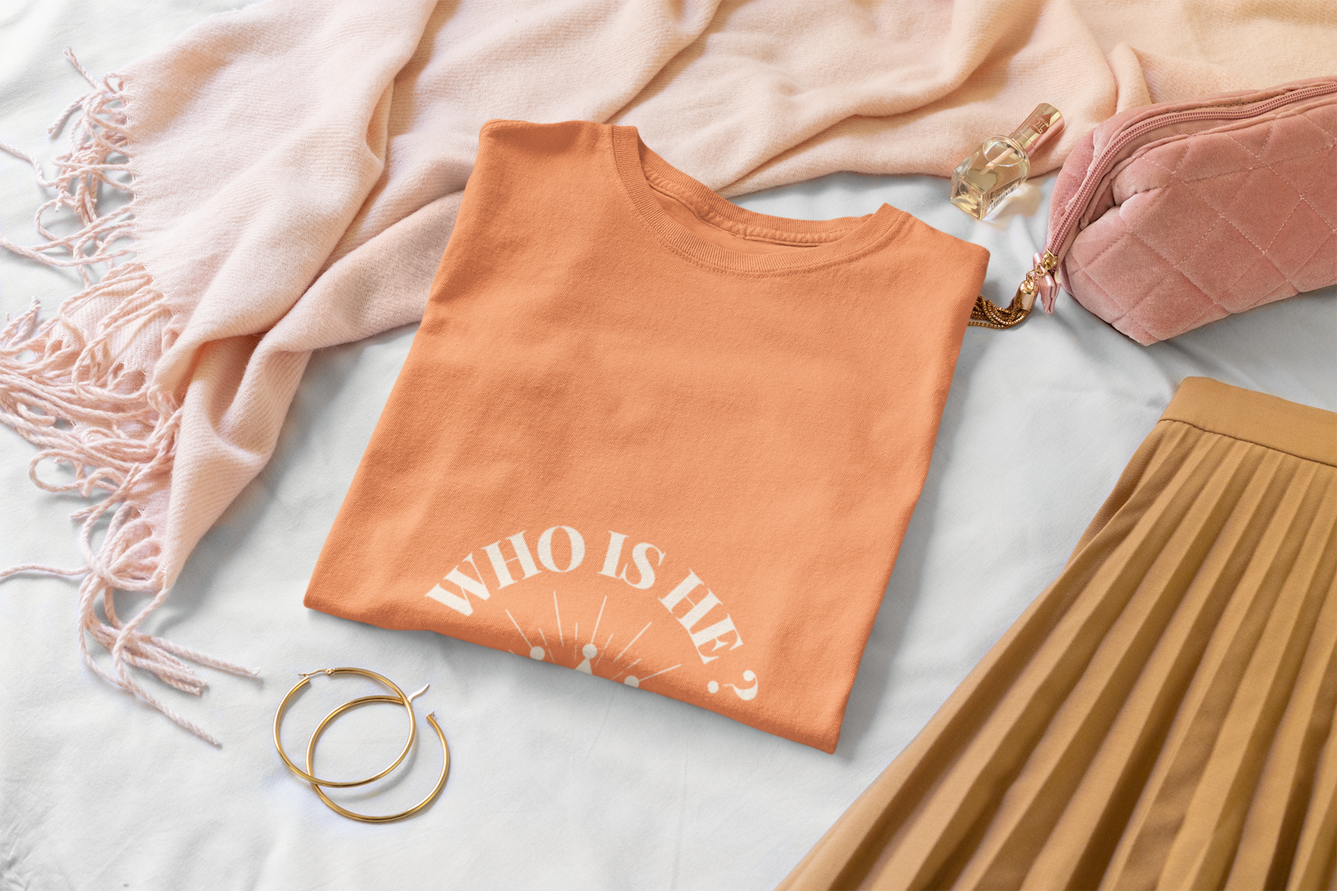 Folded orange t-shirt with 'WHO IS He?' text on a light surface with accessories.