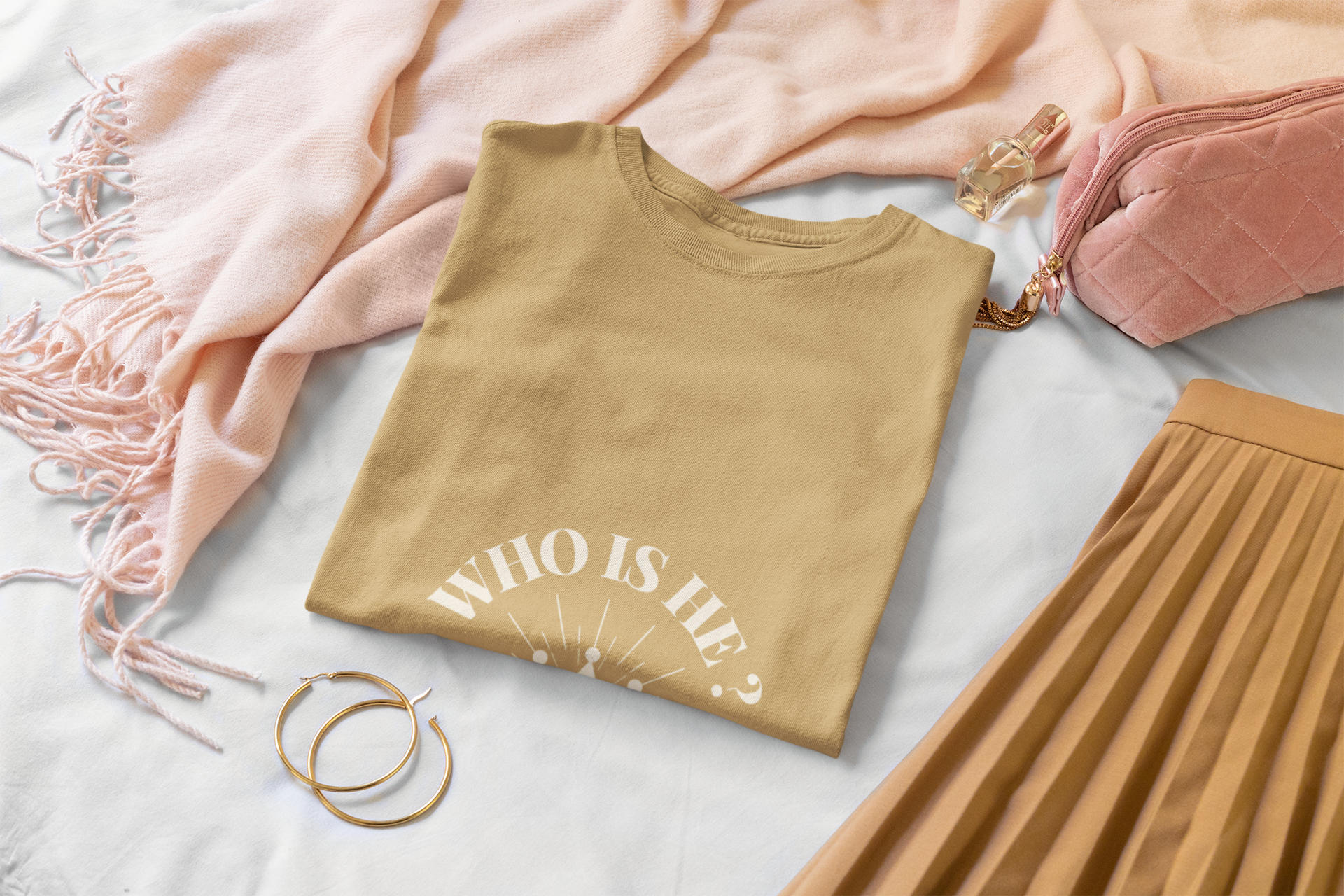 Folded golden yellow t-shirt with 'WHO IS He?' text on a light surface with pink scarf and skirt.