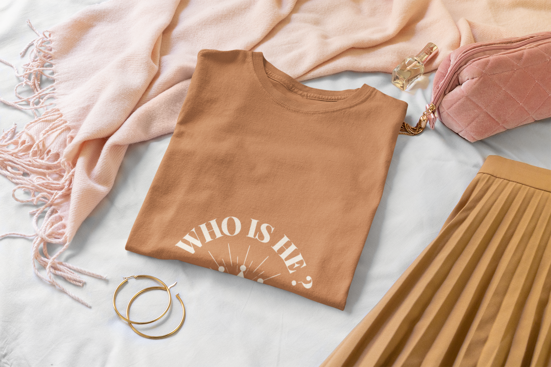 folded orange-Brown t-shirt with 'WHO IS HE?' text, pink scarf, and skirt on a light surface
