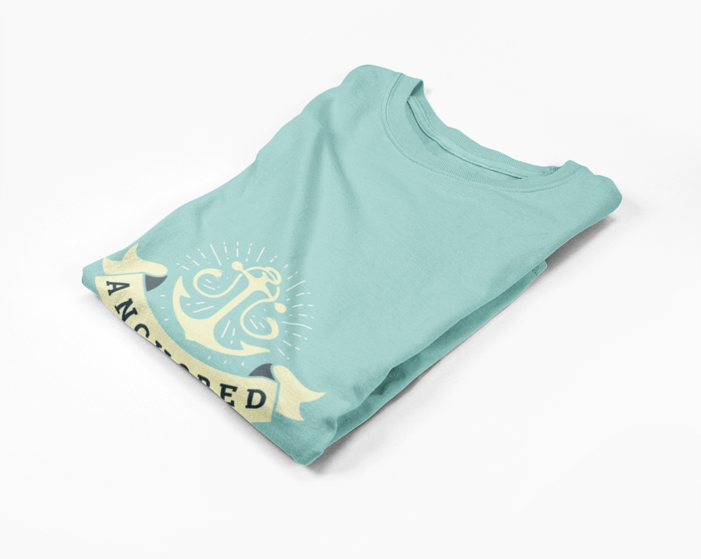 Folded light blue long-sleeve t-shirt with yellow anchor graphic and 'Anchored' text on a white background