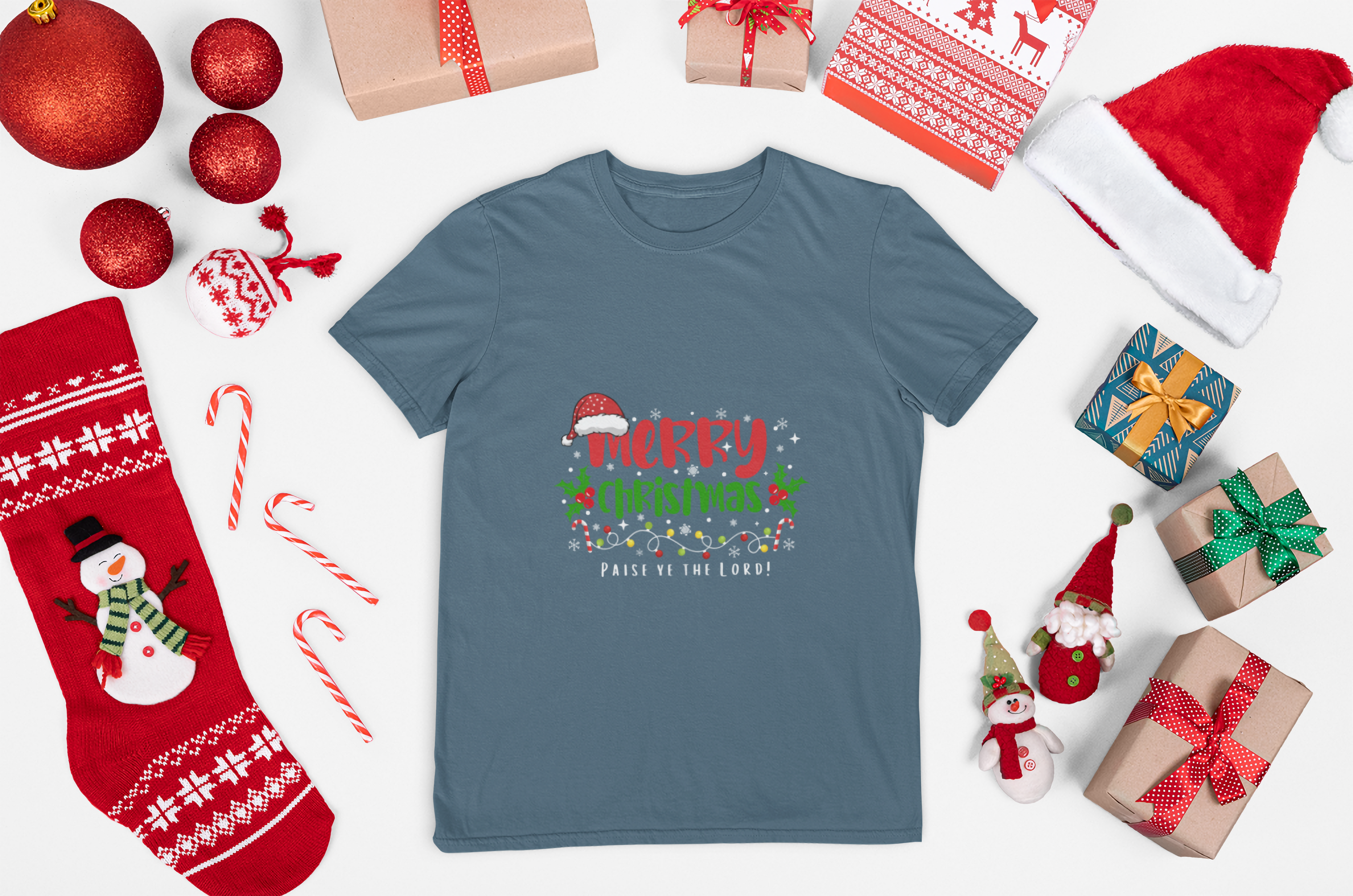 Blue t-shirt with Christmas design surrounded by festive items on a white background