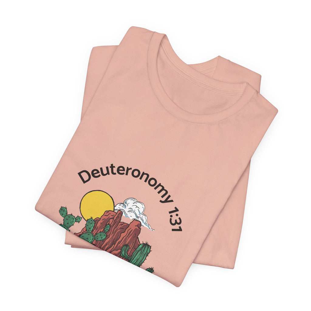 Folded pink t-shirt with desert graphic and 'Deuteronomy 13:1' text on a white background