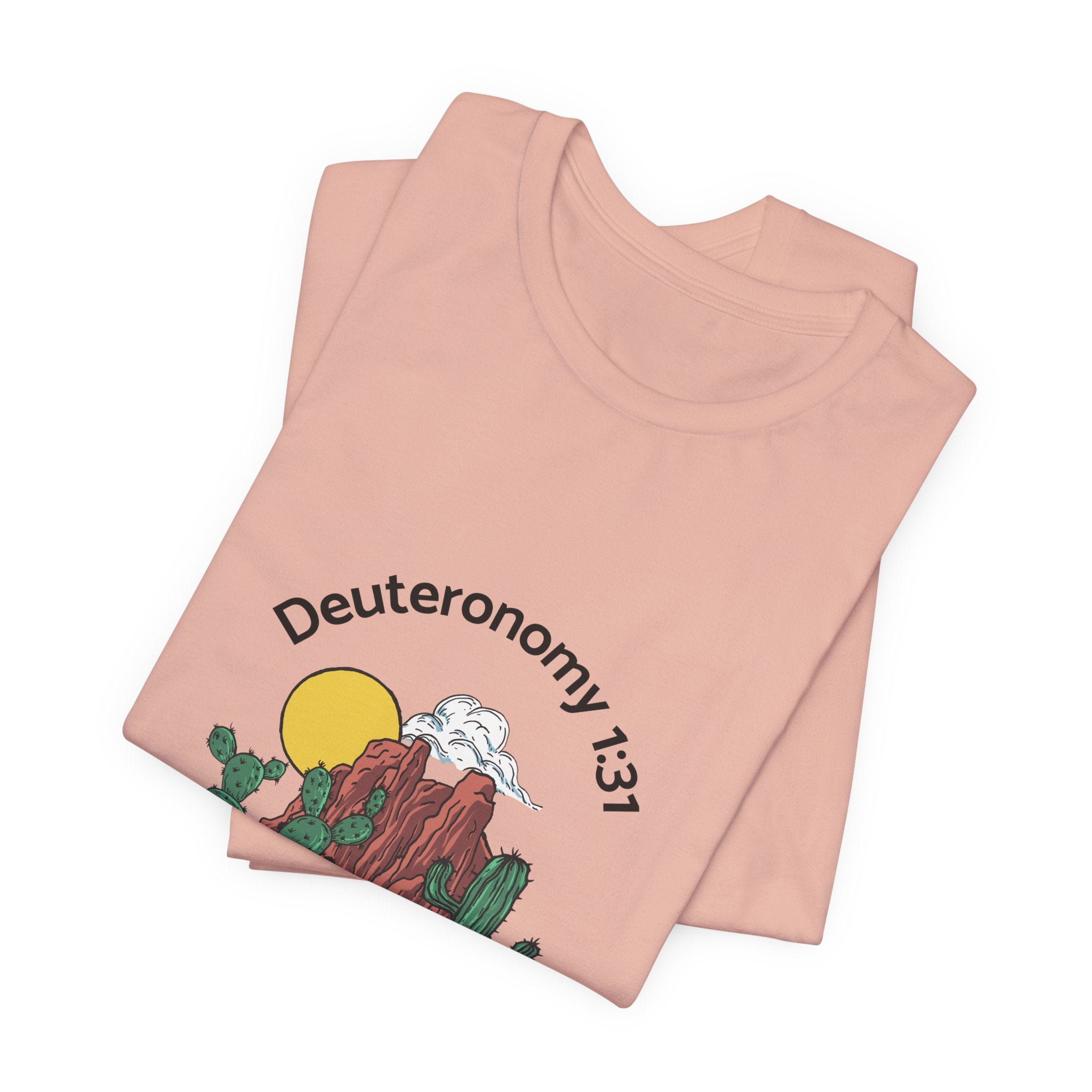 Folded pink t-shirt with desert graphic and 'Deuteronomy 13:1' text on a white background