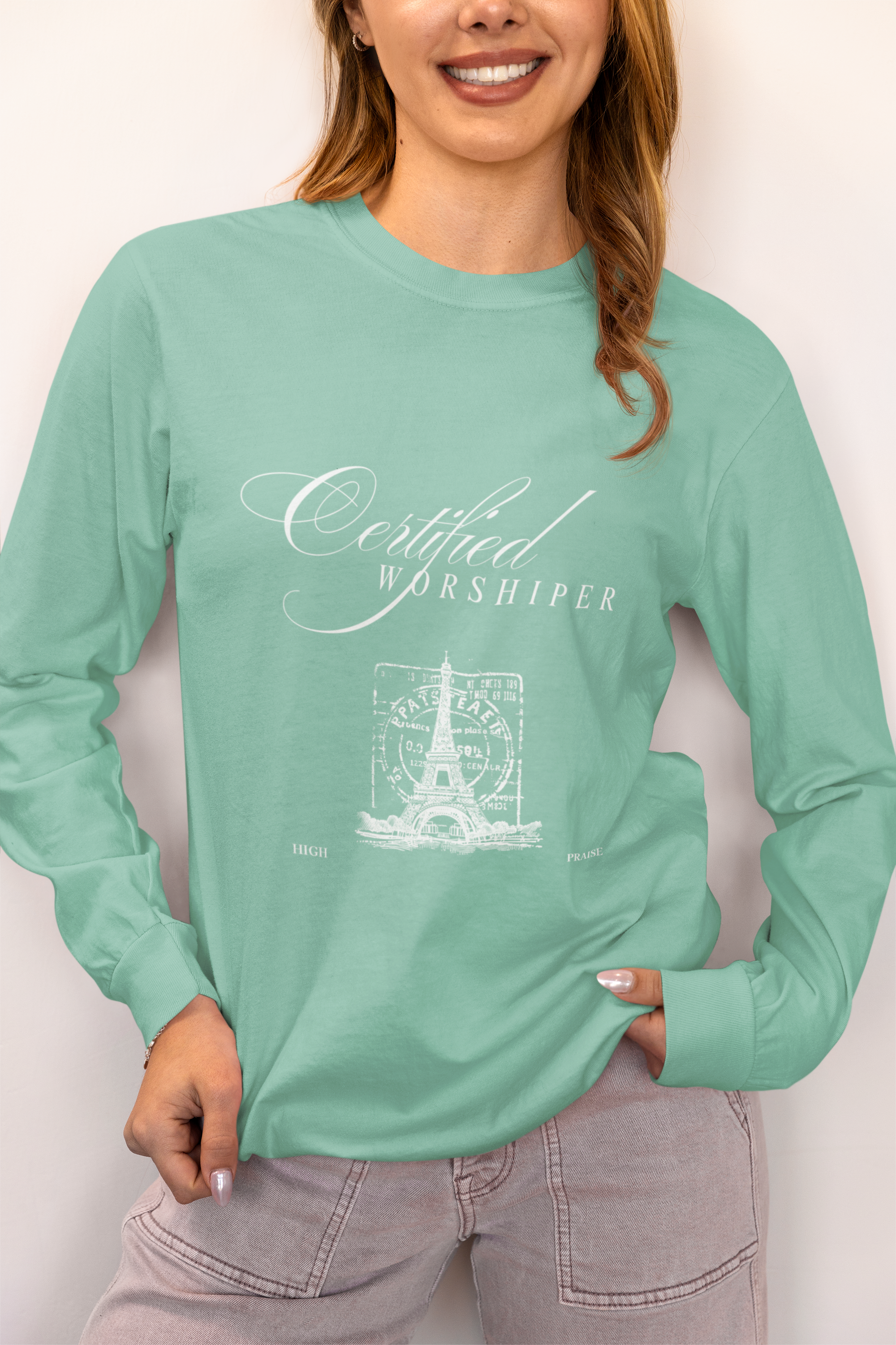 Person wearing a mint green long-sleeve shirt with 'Certified Worshipper' design on a plain background