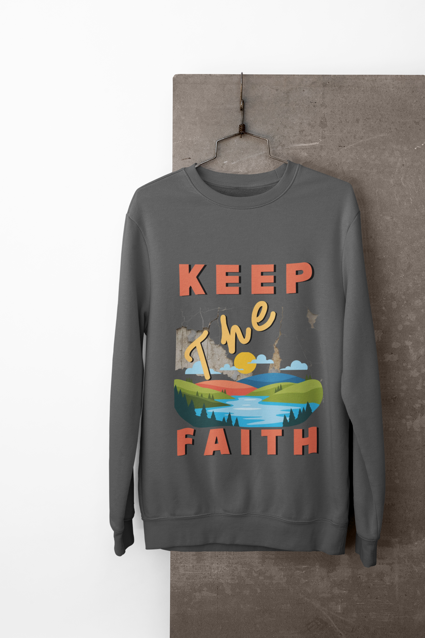 Gray sweatshirt with 'Keep The Faith' text and landscape graphic on a hanger against a neutral background