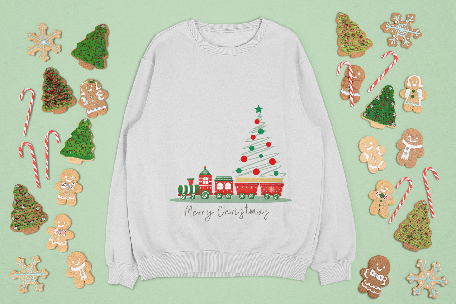 gray sweatshirt with Christmas tree and train design, surrounded by festive cookies and candy on a light green background