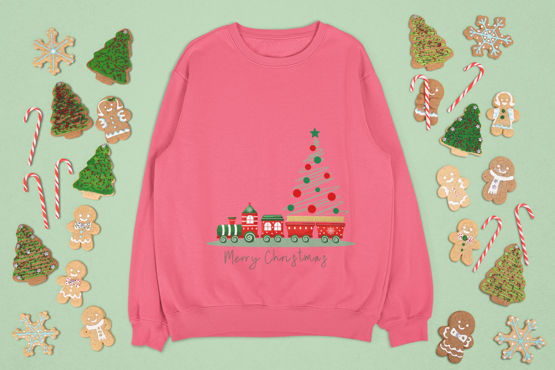 Pink sweatshirt with Christmas tree and train design on a green background with festive cookies.