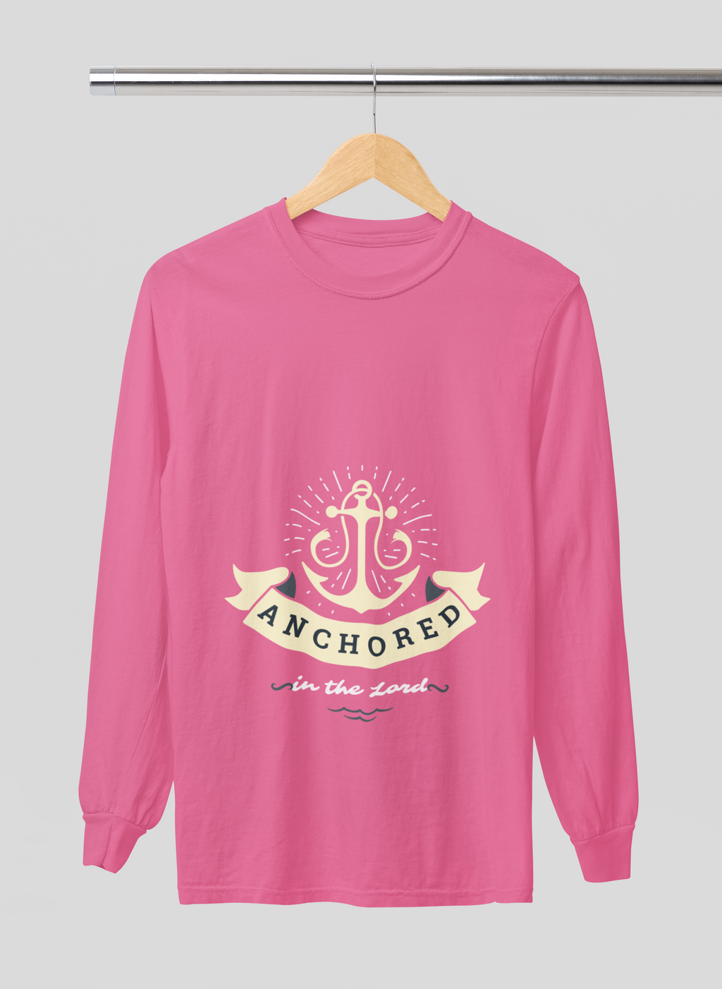 Pink long-sleeve shirt with anchor design and 'Anchored in the Lord' text on a hanger against a gray background