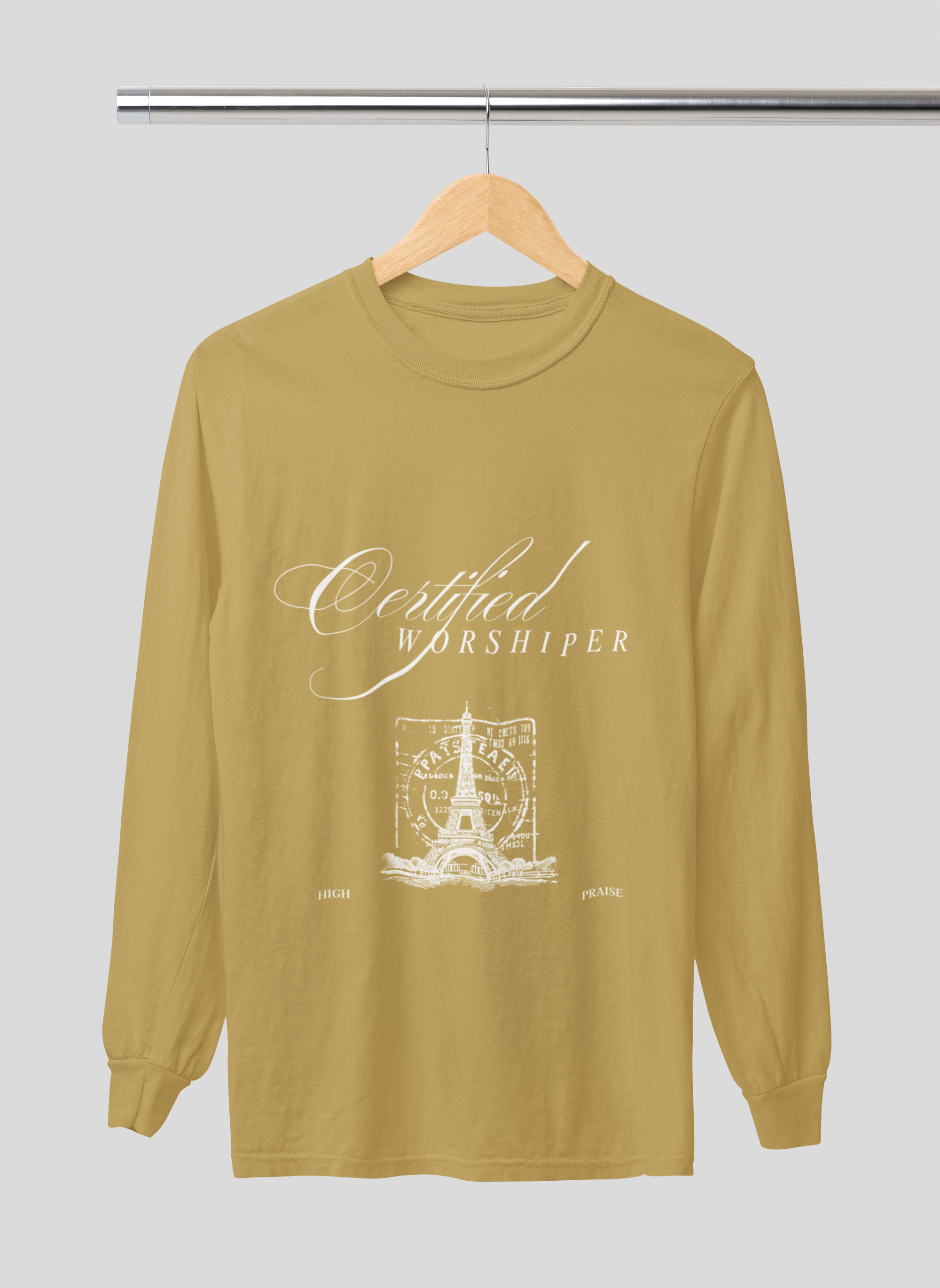 Mustard yellow long-sleeve shirt with 'Certified Worshipper' text and graphic on a hanger against a light gray background
