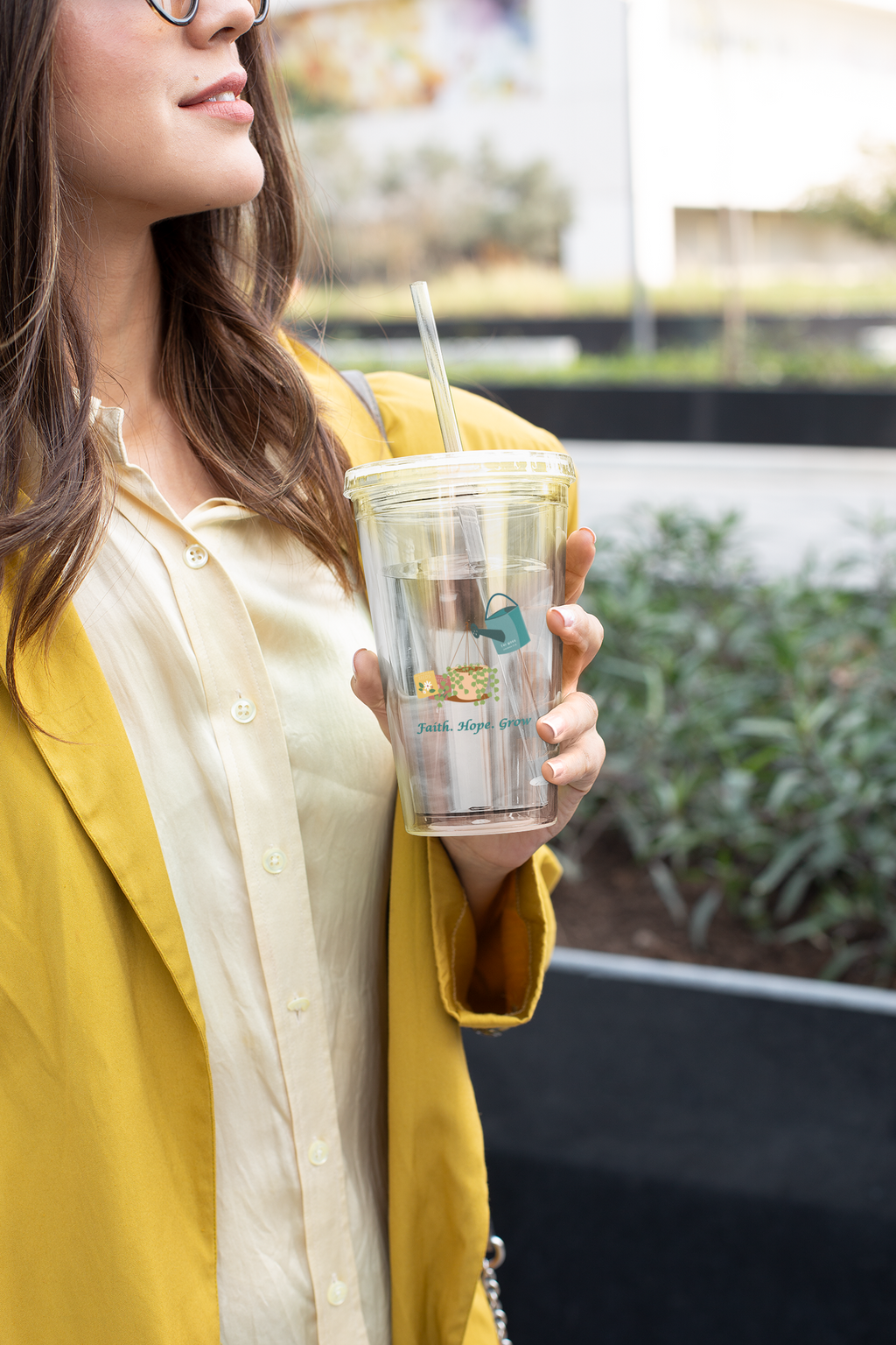 Woman holding a clear tumbler with a straw, wearing a yellow jacket.