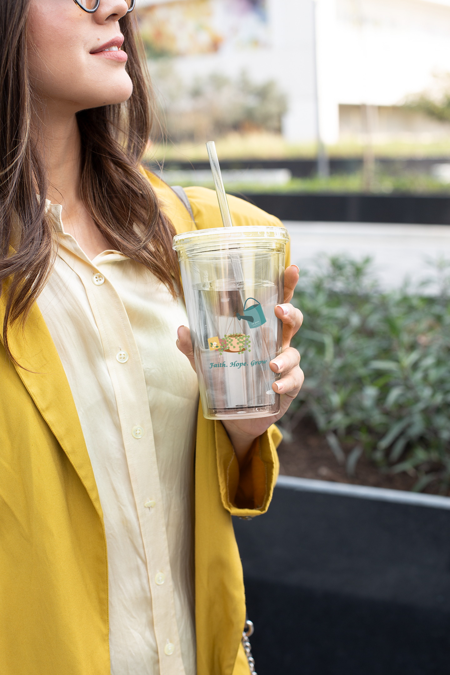 Woman holding a clear tumbler with a straw, wearing a yellow jacket.
